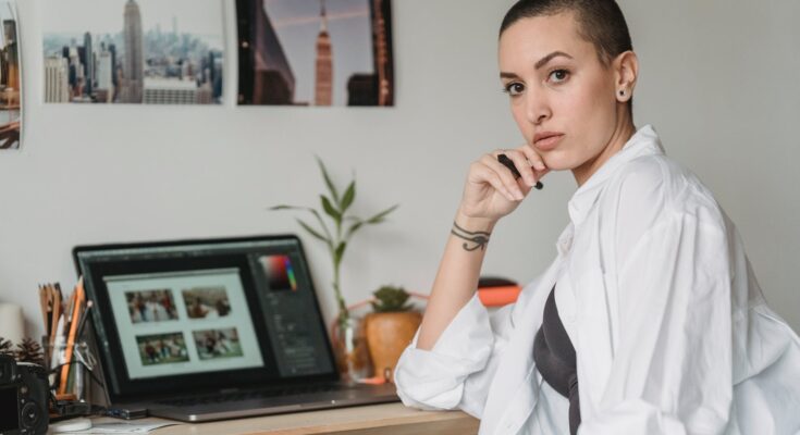 thoughtful woman with stylus working with photos on laptop