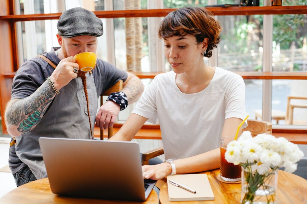 young woman using laptop while man in cap drinking coffee