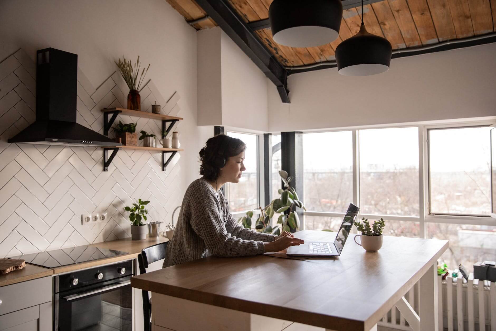 young woman surfing laptop in kitchen. Hybrid Workforce