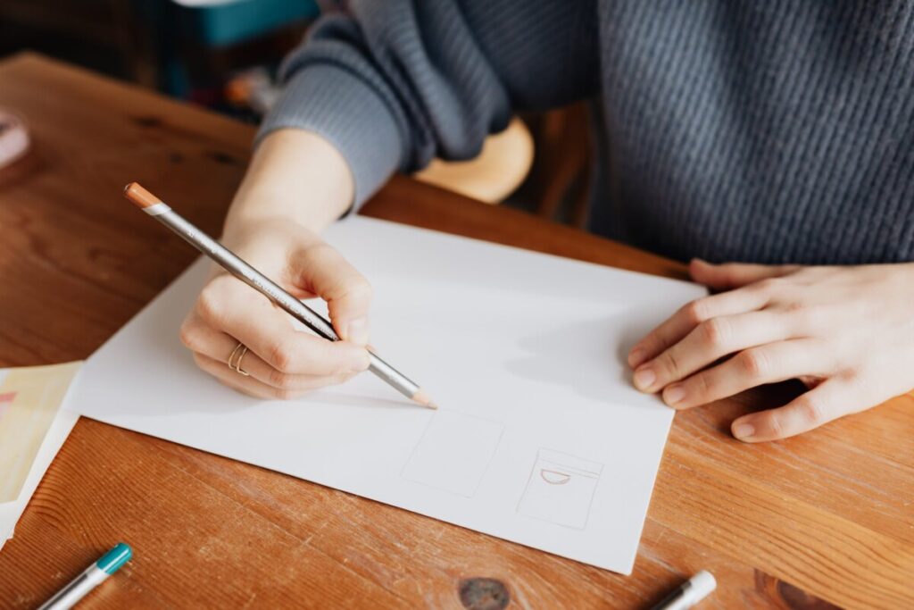 crop female designer drawing on paper sheet
