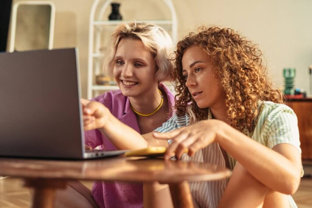 women sitting on the ground looking at the silver laptop