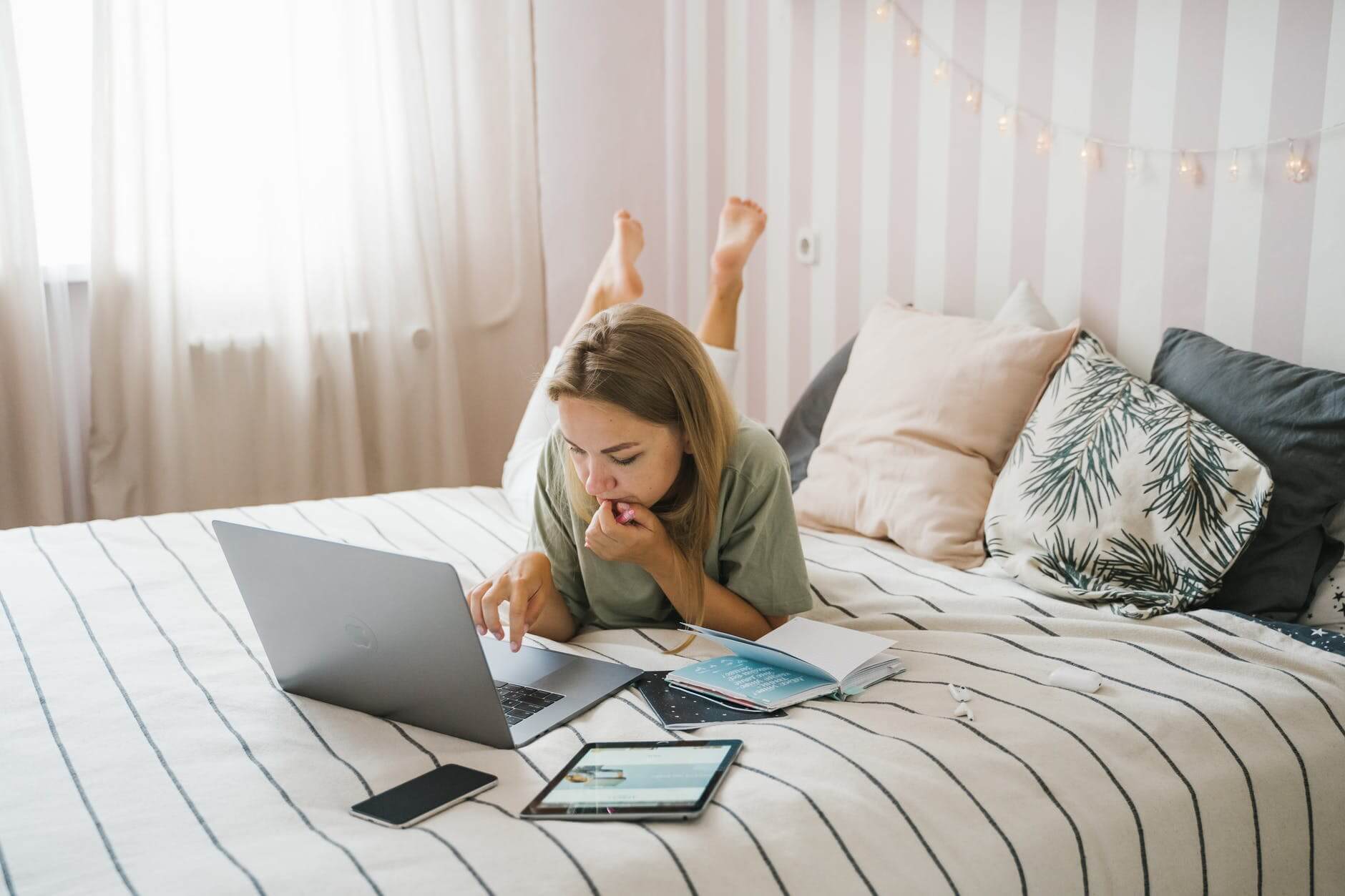 woman lying on bed while using a laptop