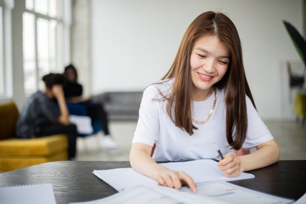 positive asian woman with notebook studying in classroom